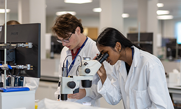 Photo of two students looking down microscopes in a lab. 